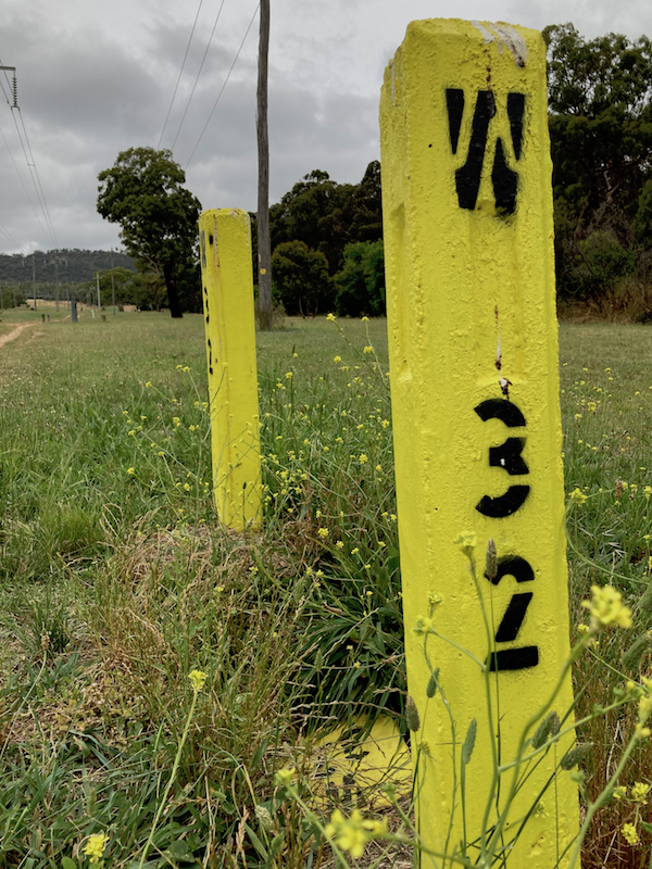 Two yellow concrete posts with black writing "W 32" stencilled on them. Overhead powerlines receding into the distance